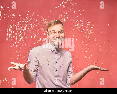 one young smiling man, 20-29 years, confetti falling down, while his arms are outs outstretched. he is looking friendly and welcoming. shot in studio  Stock Photo
