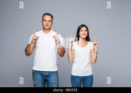 Surprised couple in casual clothes pointing with their index fingers up looking there with great astonishment isolated over white background Stock Photo