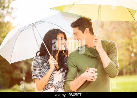 Young heterosexual couple walking in park holding hands and carrying umbrellas. Stock Photo