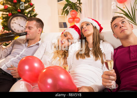Tired Friends or couple sitting on sofa after New Year's party with glass of champagne in home interior. Stock Photo