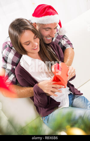 Young man gives his girlfriend a Christmas gift. She is happy while opening gift box. Stock Photo