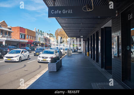 View of the high street in Botany from the pavement with shops and cars travelling through the town, Botany, Australia