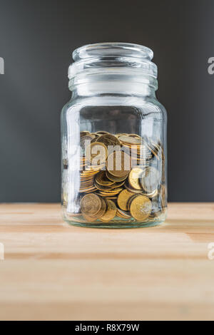 Jar with golden coins on natural wooden background. Money saving abstract concept. Stock Photo