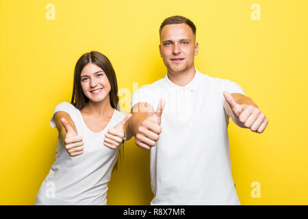 Happy young couple showing thumbs up and looking at the camera over yellow backgroun Stock Photo