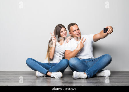 Portrait of a happy young couple sitting together over beige background, taking selfies Stock Photo