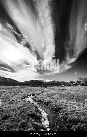 Black & white view; ranch pasture irrigation ditch; dramatic sky; Rocky Mountains; outside small town of Salida; Colorado; USA
