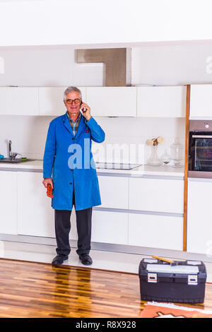 Workman standing in the kitchen, smiling and talking on mobile Stock Photo