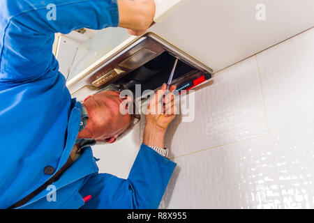 A serious male handyman is in the kitchen fixing the vent hood with screwdirver Stock Photo