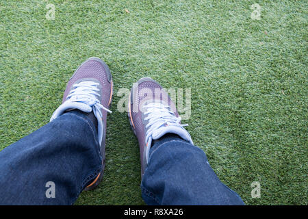 Male sneaker out of torn jeans on a green artificial grass football field. Stock Photo