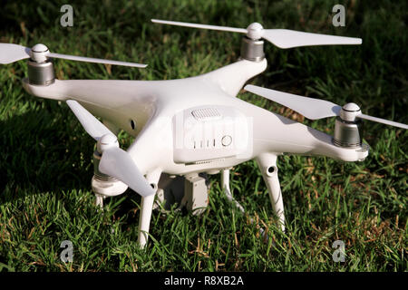 White quadcopter Drone with 4K digital camera on grass is ready for take off to fly in air to take photos, record footage from above. Drone. Stock Photo