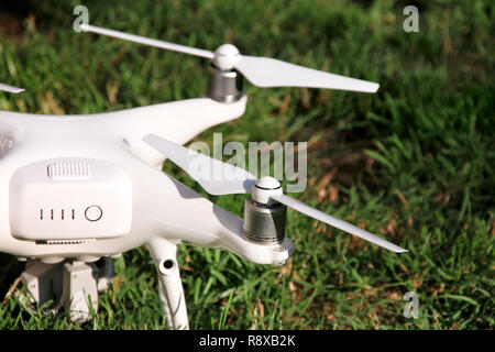 White quadcopter Drone with 4K digital camera on grass is ready for take off to fly in air to take photos, record footage from above. Drone. Stock Photo