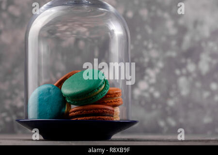 Multi-colored macarons under the glass dome on a gray background. Close-up. Delicate macarons macaroons Stock Photo