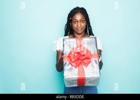 Portrait of joyous woman 20s with afro hairdo holding gift box and smiling in happiness isolated over blue background Stock Photo
