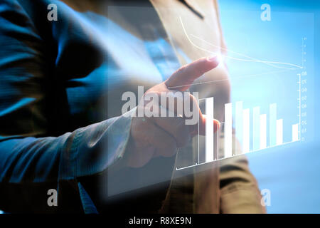 Woman pointing hologram data in business practition. Businesswomen showing a growing virtual hologram of statistics, graph and chart with arrow up on  Stock Photo