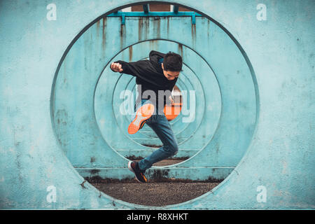 Young Asian active man jumping and kicking action, circle looping wall background. Extreme sport activity, healthy lifestyle, or parkour concept Stock Photo