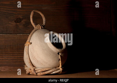 Cream colored birdhouse jug partially wrapped in a twig holder held together with leather straps. With a on a dark wooden board as its background. Stock Photo