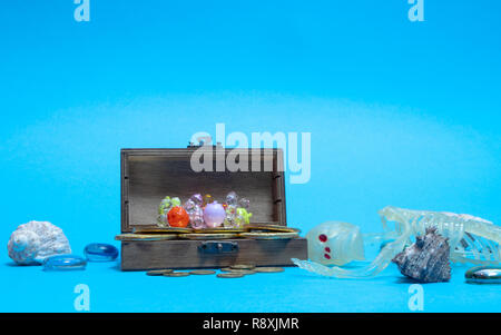 skeleton near opened wooden pirate chest with treasures, diamond, golden coins on blue background. ground view image Stock Photo