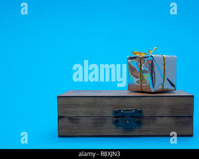 close-up small shiny silver gift box on wooden chest with blue endless background. vintage craft present concept Stock Photo