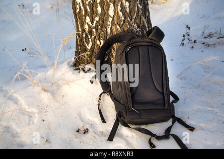 Black backpack is in the snow, comfortable heavy backpack, next to a tree Stock Photo