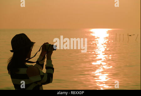 Silhouette of a woman taking pictures at the sun rising seaside Stock Photo