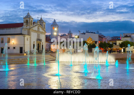 Scenic afterglow cityscape in historical city center, Illuminated fountain at the square with Santa Maria church building, Lagos, Algarve, Portugal Stock Photo