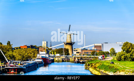 A historical Duct Windmill among the industrial buildings in the port of Rotterdam, viewed from the tourist boat on the Nieuwe Maas River in Holland Stock Photo