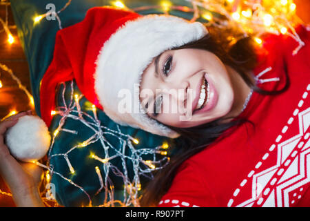 Close-up portrait of woman wrapped in christmas lights lying on floor at home Stock Photo