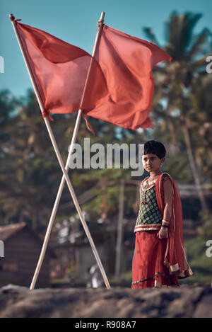 Varkala, Kerala / India – November 30, 2017: Portrait of Indian rural girl. Cute Indian girl dressed in sari, standing under red flags. Hipster color  Stock Photo