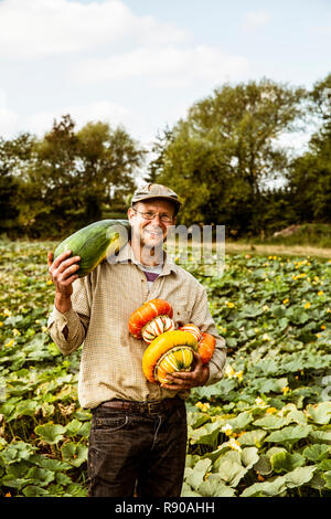Smiling farmer standing in a field, holding selection of freshly harvested pumpkins. Stock Photo