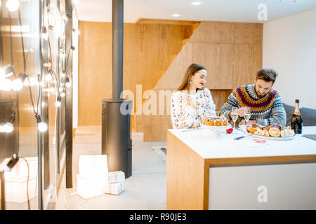 Young couple having festive dinner sitting together in the modern house during the winter holidays. Wide interior view Stock Photo