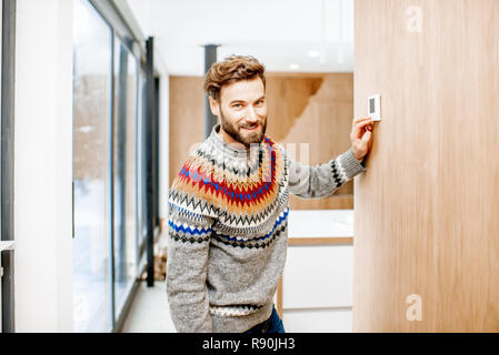 Man in sweater adjusting room temperature with electronic thermostat at home Stock Photo