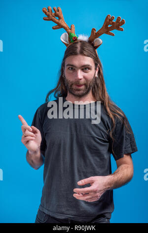 Crazy male wearing raindeer hair band making a funny grimace while pointing up with one finger. Modern Christmas accessories Stock Photo