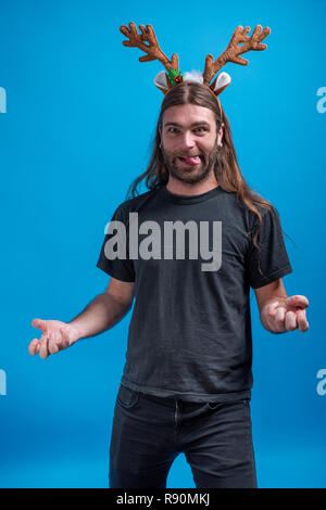 Male wearing raindeer hair band gesturing like wondering with hands and making funny face. Tongue out and looking crazy Stock Photo