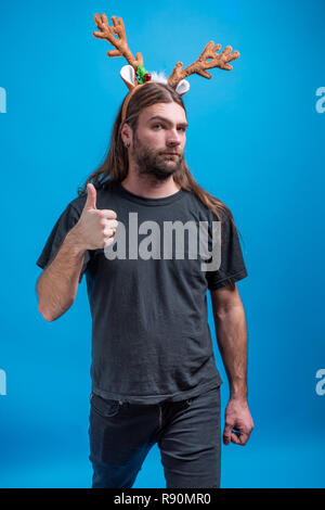 Male wearing raindeer hair band with straight face displaying thumbs up sign. Approving traditional Christmas holiday Stock Photo