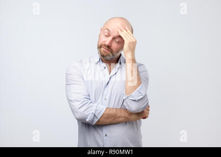 Tired and annoyed man iwith beard, leaning head on fist and breathing out from boredom Stock Photo