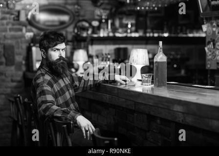 Guy spend leisure in bar, defocused background. Man with strict face sit in bar or pub near bar counter. Hipster with beard ordered drinks, waits for friends. Rest and relax concept. Stock Photo