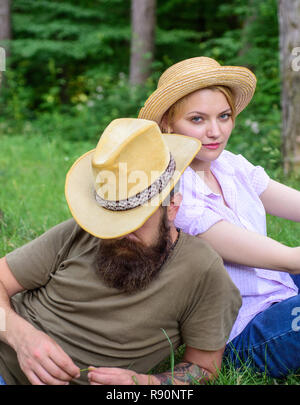 Couple in straw hats sit meadow relaxing. Choose proper clothing and equipment to hike and forest picnic. Couple tourists wearing hats. Reasons you should definitely wear more hats. Hats for tourism. Stock Photo