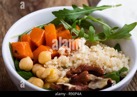 Healthy salad bowl with baked pumpkin,  chickpeas, quinoa, arugula, walnuts and yogurt dressing on rustic wooden table, selective focus Stock Photo