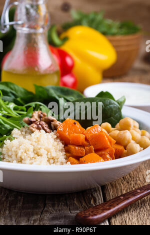 Healthy salad bowl with baked pumpkin,  chickpeas, quinoa, arugula, walnuts and yogurt dressing on rustic wooden table, selective focus
