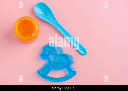 Jar of baby food, spoon and teether on pink background. Child's teething, nutrition and growing up. Stock Photo