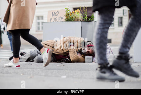 A homeless beggar man lying on the ground outdoors in city, sleeping. Stock Photo