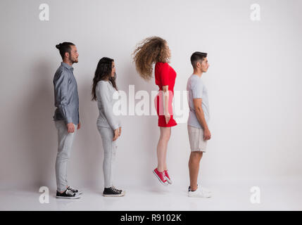 Side view of young group of friends standing in a studio, one is jumping. Stock Photo