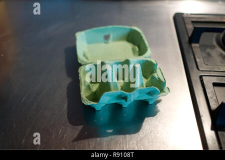 an open empty green cardboard egg box lies on a stainless steel kitchen work surface next to a gas hob Stock Photo