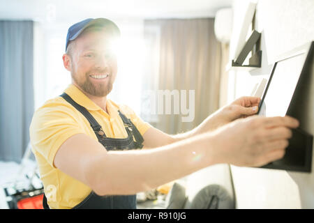 Jolly handyman in cap putting frame on shelf Stock Photo
