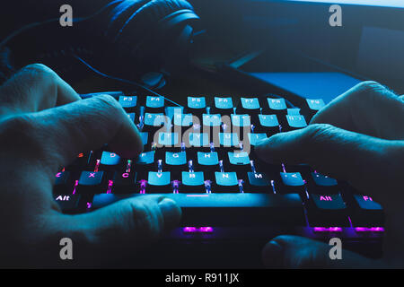 Male hands typing on the black illuminated keyboard with blue light coming from screen Stock Photo