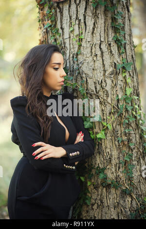 Beautiful young woman arms crossed leaning against a tree Stock Photo