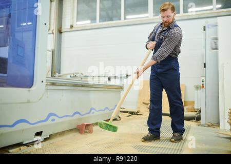 Young man in workwear sweeping floor Stock Photo