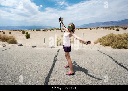 Young adult female photographer on a road trip through Death Valley National Park, stands and stretches her arms and legs Stock Photo