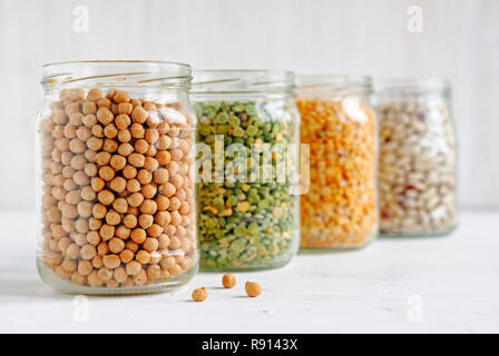 Glass jar of healthy dried chickpeas in a receding line with other jars of legumes over a white background Stock Photo
