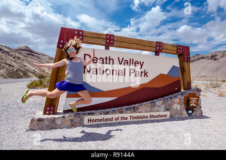 AUGUST 4 2018 - DEATH VALLEY, CALIFORNIA: Sign for Death Valley National Park on an overcast summer day.. Woman jumps and poses next to sign Stock Photo